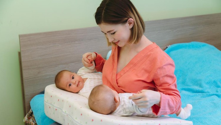 Happy mother lying in bed with baby daughters in the morning
