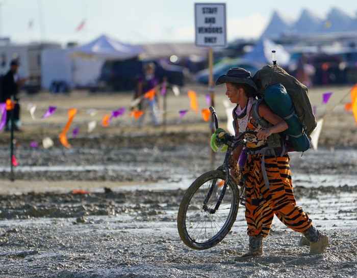 A Burning Man participant walks their bike through the mud near the exit, after a severe rainstorm left tens of thousands of revelers attending the annual festival stranded in mud in Black Rock City, in the Nevada desert September 3, 2023.  Trevor Hughes/USA Today Network via REUTERS.   MANDATORY CREDIT. NO RESALES. NO ARCHIVES