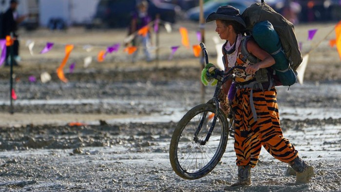A Burning Man participant walks their bike through the mud near the exit, after a severe rainstorm left tens of thousands of revelers attending the annual festival stranded in mud in Black Rock City, in the Nevada desert September 3, 2023.  Trevor Hughes/USA Today Network via REUTERS.   MANDATORY CREDIT. NO RESALES. NO ARCHIVES