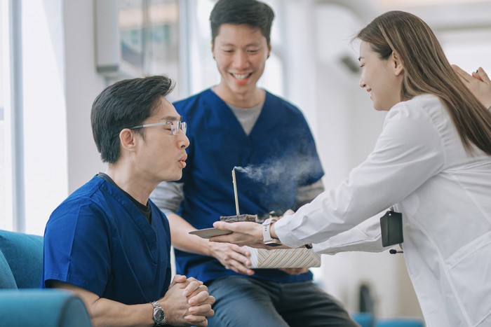 Asian Chinese male nurses blowing birthday candle light celebration in clinic with colleague