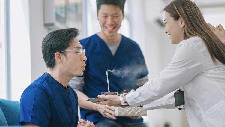 Asian Chinese male nurses blowing birthday candle light celebration in clinic with colleague