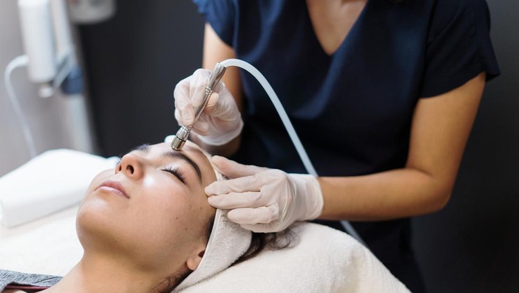 1372582333 A young latin woman getting a facial treatment with a device.