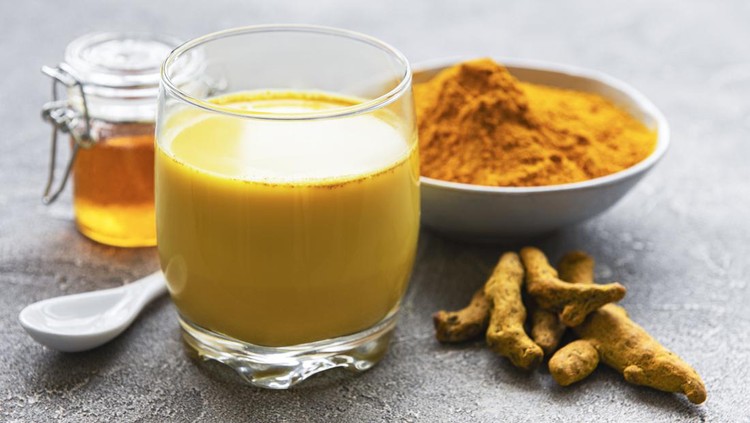 1254503729 Yellow turmeric latte drink. Golden milk with cinnamon, turmeric, ginger and honey over grey concrete background.
