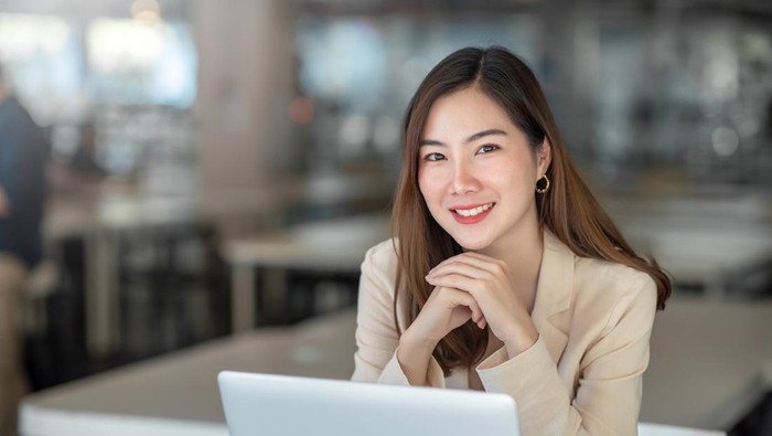 Charming Asian businesswoman working with a laptop at the office. Looking at camera.