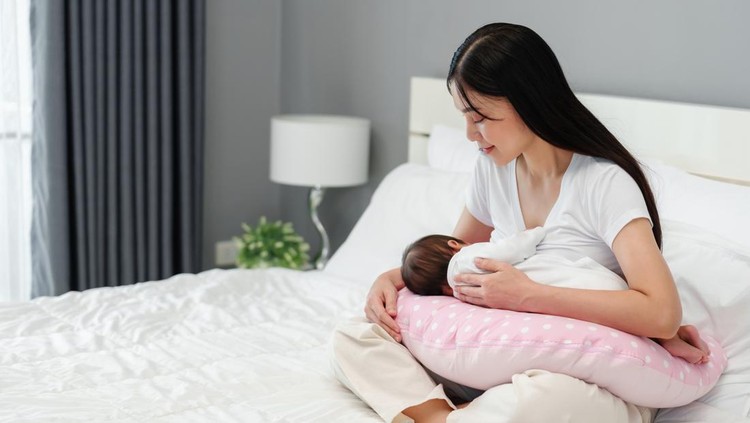 mother breastfeeding newborm baby on a bed