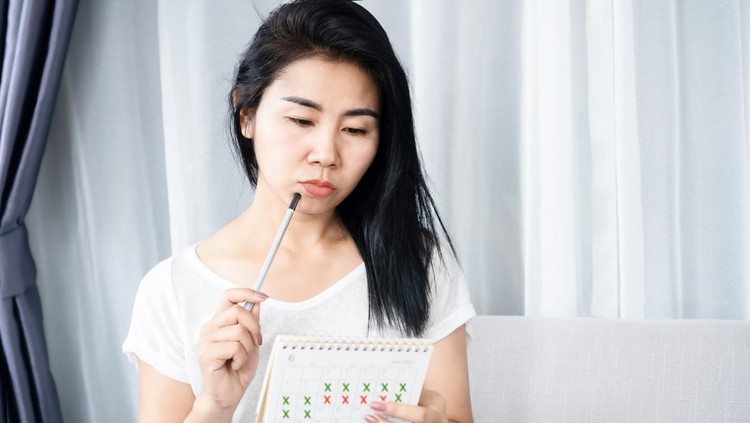 Asian woman having problem with amenorrhea, irregular periods and counting her menstrual cycles on calendar