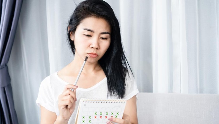 jadwal haid Asian woman having problem with amenorrhea, irregular periods and counting her menstrual cycles on calendar