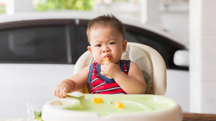 the baby learns to eat by himself. he can use spoon well. so he is very happy (focus at his face)