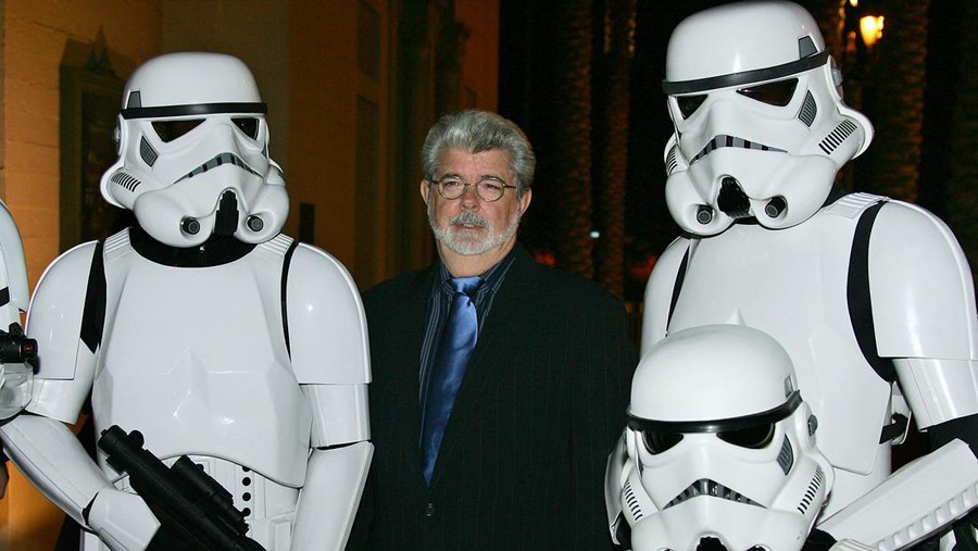 George Lucas TOPSHOT - Star Wars creator George Lucas poses with characters from the famed movie as he arrives for the Jules Verne Adventure Film Festival & Exposition launch event, 06 October 2006 at the Shrine Auditorium in Los Angeles, California. (Photo by Robyn BECK / AFP) (Photo by ROBYN BECK/AFP via Getty Images)
