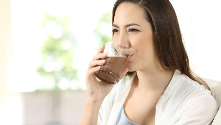 Happy woman drinking a cocoa shake sitting on a couch in the living room at home