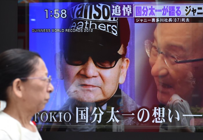 A woman walks past a roadside television screen reporting the death of Johnny Kitagawa, founder of Japanese talent agency Johnny & Associates Inc., in Tokyo on July 10, 2019. - Japan's leading boyband star-maker Johnny Kitagawa, who built an entertainment empire and broke records with his acts, has died of a stroke on July 9, his company said. He was 87. (Photo by Kazuhiro NOGI / AFP)        (Photo credit should read KAZUHIRO NOGI/AFP via Getty Images)