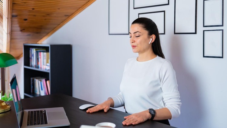 Relaxed calm business woman take deep breath of fresh air resting with eyes closed at work in home office. Doing office yoga and meditating with closed eyes.