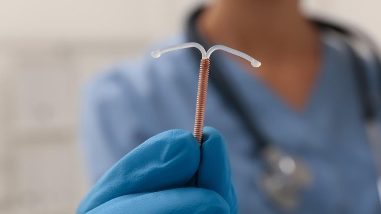 Doctor holding T-shaped intrauterine birth control device on blurred background, closeup