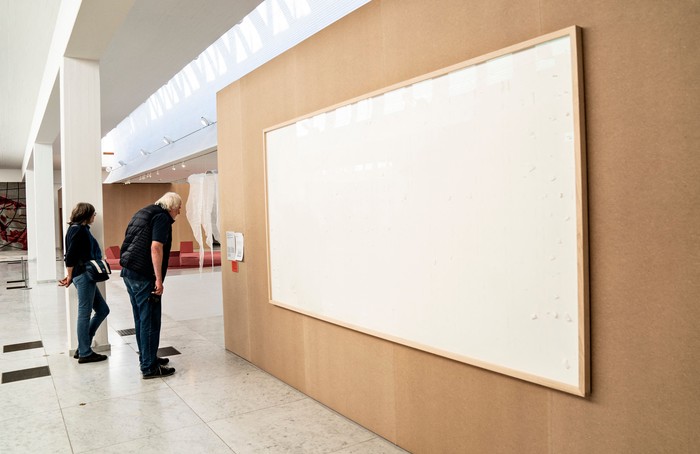 People stand in front of an empty frame hung up at the Kunsten Museum in Aalborg, Denmark, on September 28 2021. - The Danish museum loaned an artist $84,000 in cash to recreate old artworks of his using the banknotes, but the boxes he sent only contained blank canvasses and a new title: 
