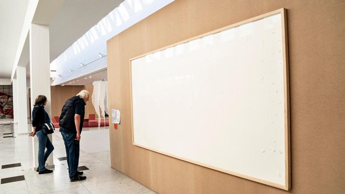 People stand in front of an empty frame hung up at the Kunsten Museum in Aalborg, Denmark, on September 28 2021. - The Danish museum loaned an artist $84,000 in cash to recreate old artworks of his using the banknotes, but the boxes he sent only contained blank canvasses and a new title: 