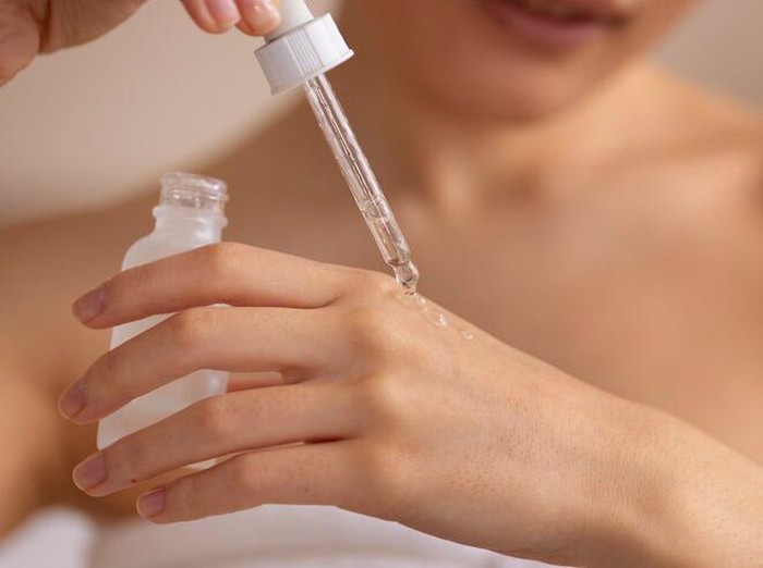 Foto perempuan menggunakan serum tubuh