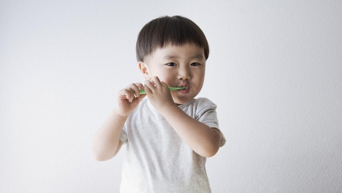 An asian boy brushing his teeth.
