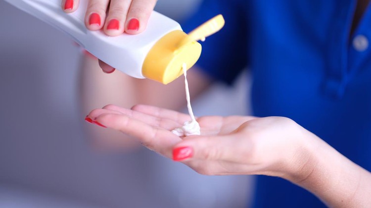 Woman pours body care lotion or sunscreen from bottle into hand&period; Moisturizing and protecting skin concept&period;
