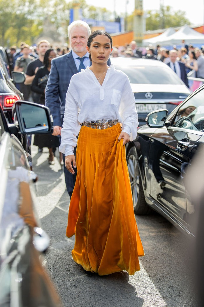 Yara Shahidi menunjukkan bahwa gaya yang simple sangat cocok untuk acara Dior. Pleated skirt berwarna oranye terlihat serasi dengan white blouse/ Foto: Getty Images/Christian Vierig