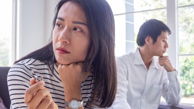 The concept says goodbye to the problem of divorce in love. Asian couples are having conflicts. The wife is taking off the wedding ring behind a stressed husband and family problems.