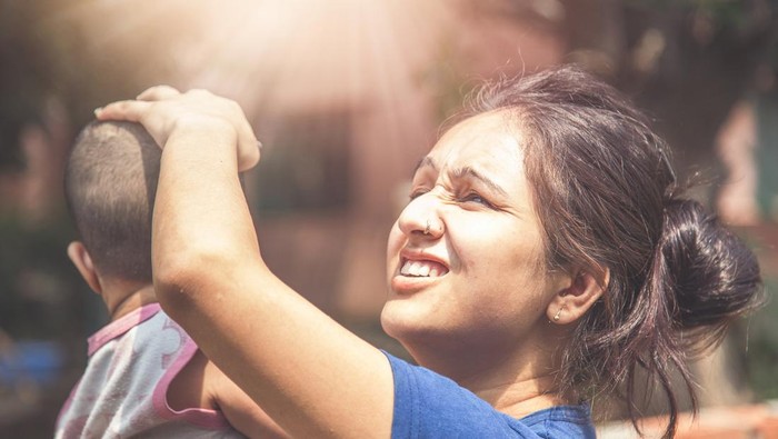 Indian kid and mother standing outside in sunlight during hot summer season