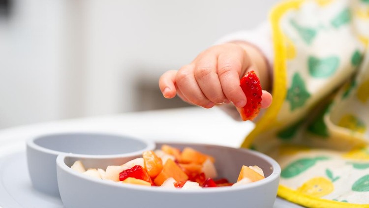 Macro Close up of Baby Hand with a Piece of Fruits Sitting in Child's Chair Kid Eating Healthy Food
