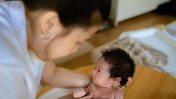 Mother bathing his baby in bathroom and than dressing in bedroom at home.