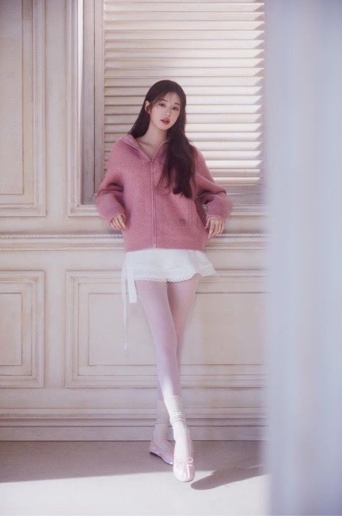 Jika tidak suka memakai baju ketat, kamu bisa mencontek gaya Jang Wonyoung IVE berikut ini. Padukan jaket longgar berwarna pastel dengan rok flowy dan tights putih. Leg warmer dan ballet flat juga bisa membuatmu tampil lebih feminin./ Foto: Koreaboo.com