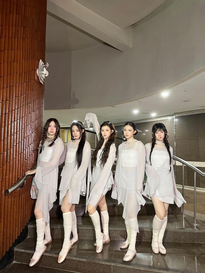 NewJeans tampil elegan dengan outfit bahan sifon yang flowy, kaus kaki panjang putih, dan ballet flat kala membawakan lagu Cool With You. Hiasan rambut pita kecil juga bisa menambah kesan manis./ Foto: Facebook/NewJeans