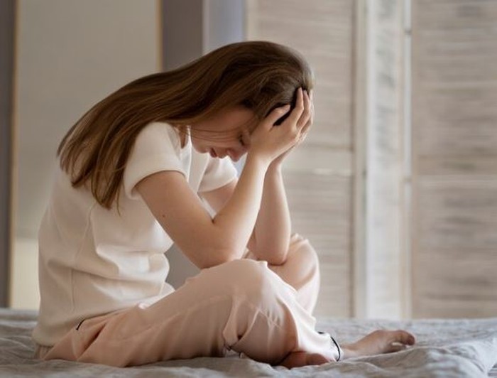 Perempuan menunduk di atas kasur terlihat sedih