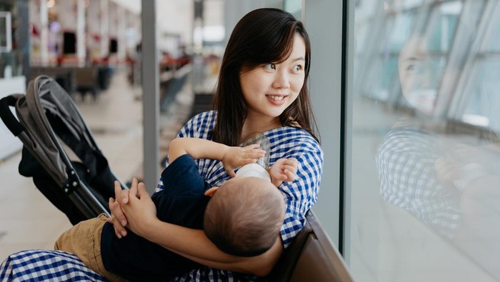 An Asian Chinese woman feeding her baby while waiting for flight at the airport
