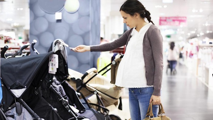 Beautiful young pregnant mother choosing and buying colorful clothes and appliances for her new incoming baby in. Child shop or store concept.