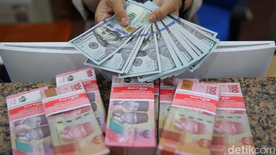 Teller bank menghitung uang Dollar diatas tumpukan Rupiah.