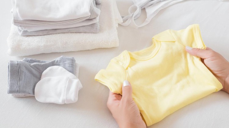 Woman's hands sorting new baby clothes on white bed sheet. Mother's daily duties. Soft colors. Closeup.