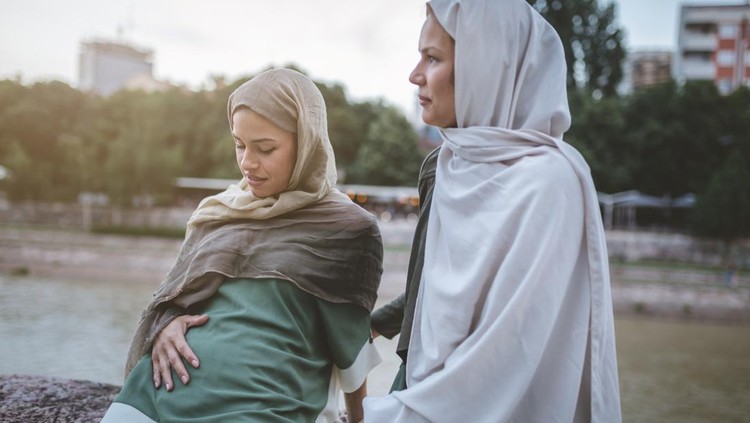 Cute and lovely pregnant Muslim woman and her Muslim friend, spending the time together on a city street.