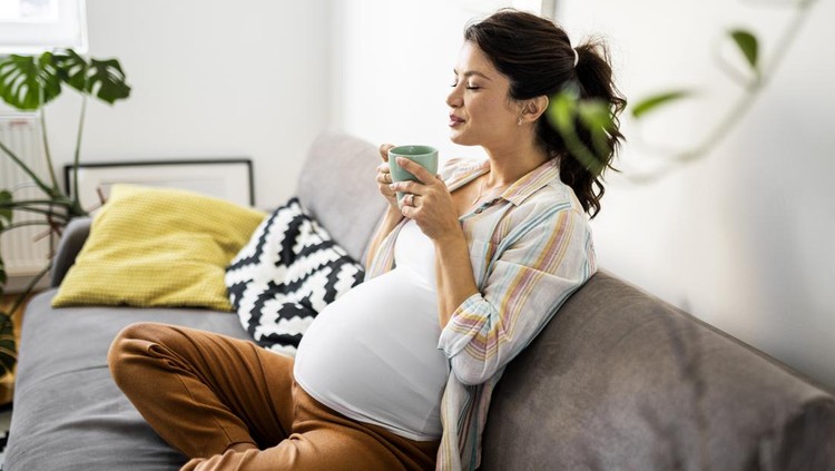 Pregnant woman resting on sofa holding cup of coffee