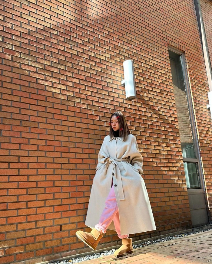 Untuk melengkapi gaya kasual dan chic, Mimi memilih wrap coat dan boots coklat yang memberikan sentuhan edgy. Ia memadukan tampilannya dengan celana pink yang kontrast, menciptakan ensemble antara keanggunan dan keberanian./ Foto: fmkorea.com