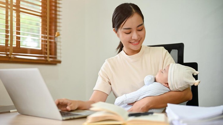 ilustrasi working mom Young beautiful Asian mother working at home and holding her baby in her arms.
