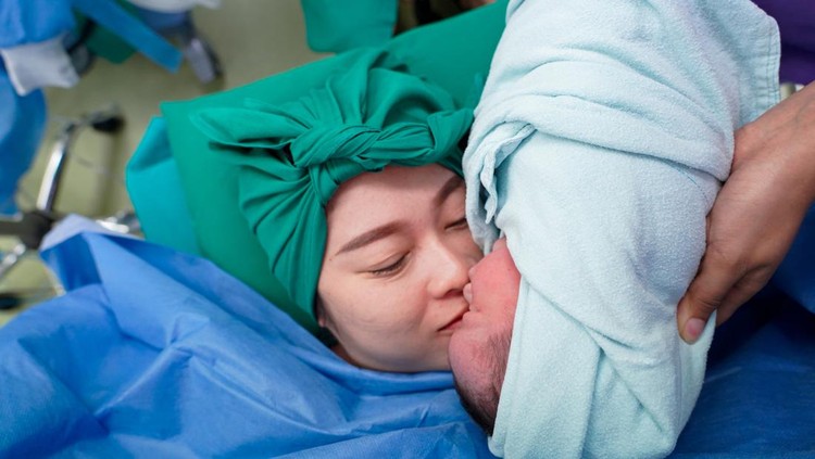 Newborn baby in delivery room.Blurred Mother background giving birth to a baby and kiss her baby. Woman pregnant patient in a hospital. Parent and infant first moments of bonding.