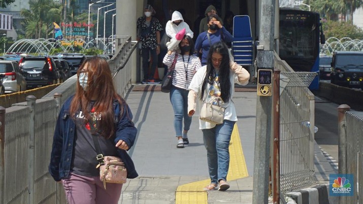 Pejalan kaki menggunakan payung untuk menghindari terik matahari di kawasan Jembatan Pinisi di halte busway Karet, Jakarta, Selasa (19/12/2023). (CNBC Indonesia/Muhammad Sabki)