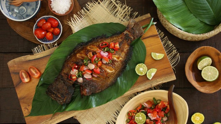 Ikan Bakar Dabu-Dabu, the popular grilled fish dish from Manado, North Sulawesi. The fish is lightly seasoned then grilled; served with the spicy tomato salsa. The fish is plated on a wooden serving block lined with layers of broad green leaves. Accompanied with extra salsa and limes.