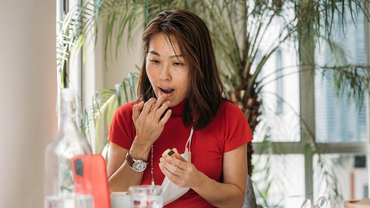 An Asian Chinese woman putting on lip balm using smartphone as a mirror at office.