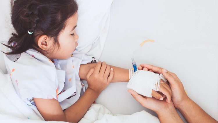 923552574 Mother hand holding sick daughter hand who have IV solution bandaged with love and care while she is sleeping on bed in the hospital