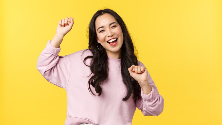 People emotions, lifestyle leisure and beauty concept. Upbeat happy and cheerful asian girl dancing and having fun, partying, moving rhythm music and smiling over yellow background.