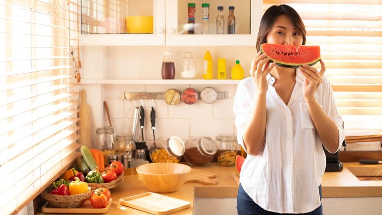 Girl eating watermelon in the kitchen.