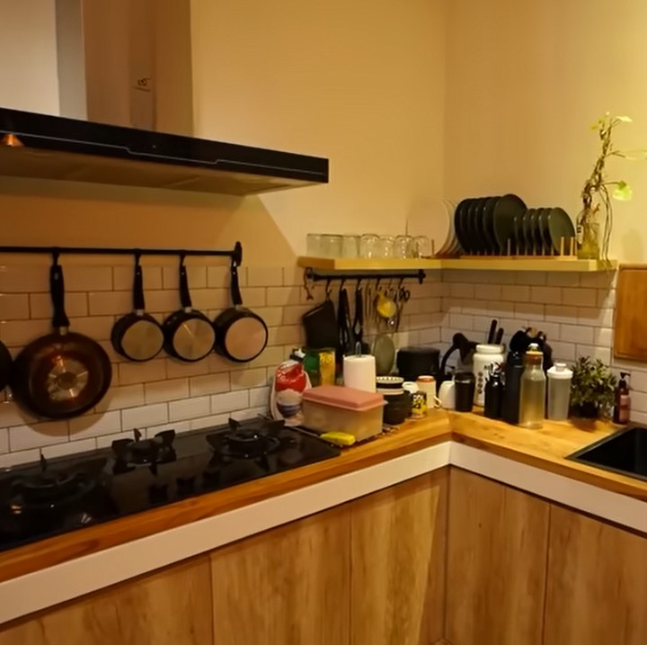 <p>Bagian dapur rumah Dikta terasa hangat dengan nuansa kayu dan lampu temaram. Di sebelah dapur, terdapat meja kecil dengan dua kursi minimalis. (Foto: YouTube Taulany TV)</p>