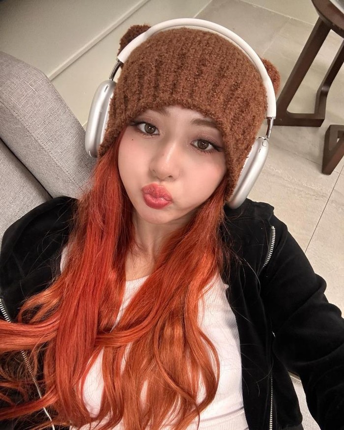 Yunjin LE SSERAFIM memamerkan gaya Gen Z yang trendi dengan beanie telinga kucing dan headset. Dipadukan dengan warna rambut oranye, ia terlihat unik seperti karakter dalam sebuah game./ Foto: Elle.co.kr