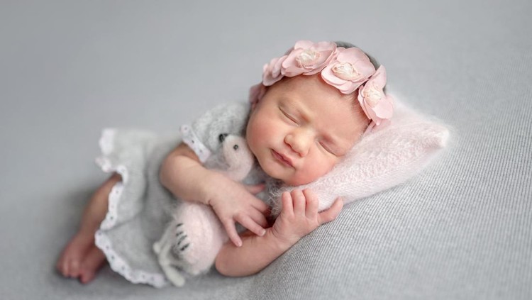Newborn Girl Sleeps In Gray Dress With Flamingo Toy During Baby Photoshoot In Studio