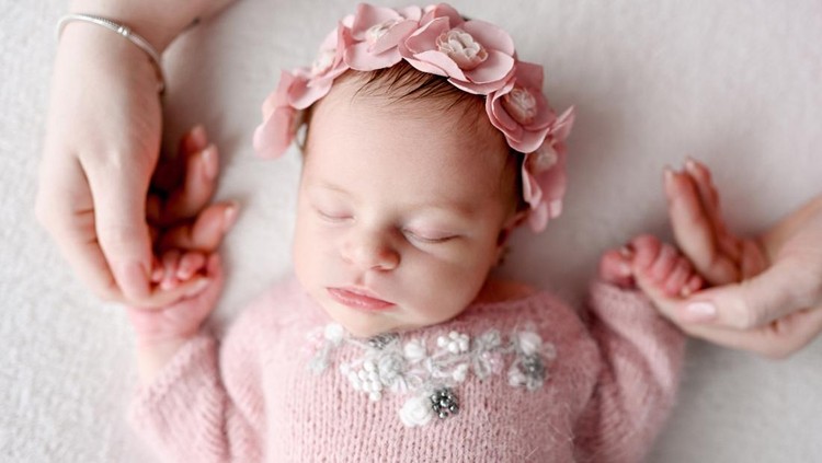 Newborn baby girl wearing flower wreath sleeping and mother holding her hands. Infant child kid napping, parent care and love
