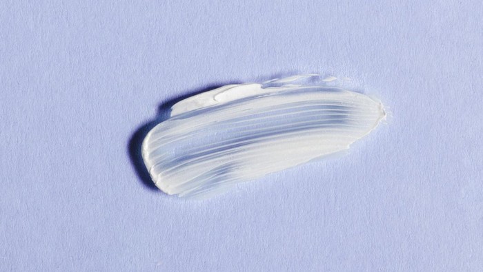 White skin cream smear on violet background. Skincare cosmetics concept with moisturizing beauty product for facial cleanse or body SPA